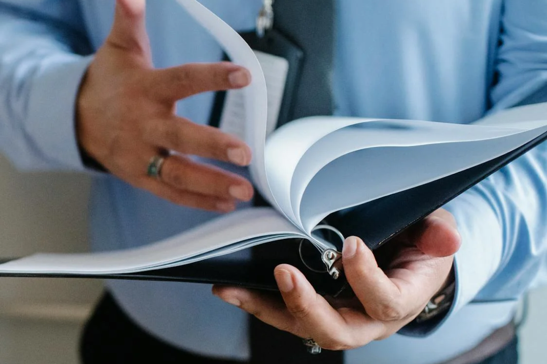 Professional reviewing documents in a binder, representing the process of achieving ISO 27001 certification for enhanced information security and compliance.