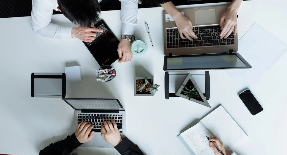 Overhead view of professionals working on laptops and documents, representing collaborative efforts to achieve ISO 27001 certification for enhanced information security